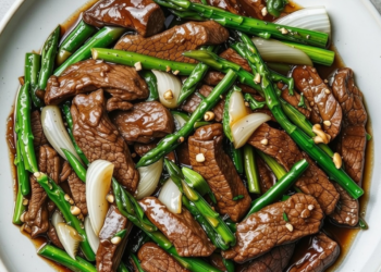 Oosterse wokschotel met biefstuk, groene asperges en ui in oestersaus