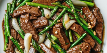 Oosterse wokschotel met biefstuk, groene asperges en ui in oestersaus